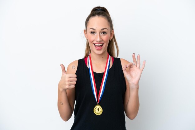Jonge blanke vrouw met medailles geïsoleerd op een witte achtergrond met ok teken en duim omhoog gebaar