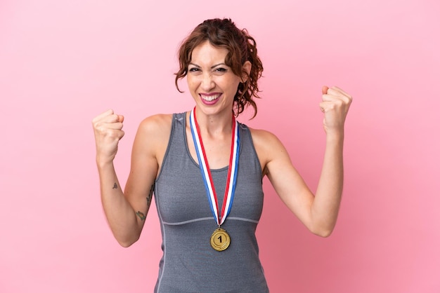 Foto jonge blanke vrouw met medailles geïsoleerd op roze achtergrond die een overwinning viert