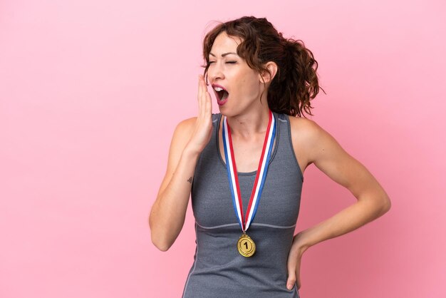 Jonge blanke vrouw met medailles geïsoleerd op roze achtergrond geeuwen en wijd open mond met hand bedekken