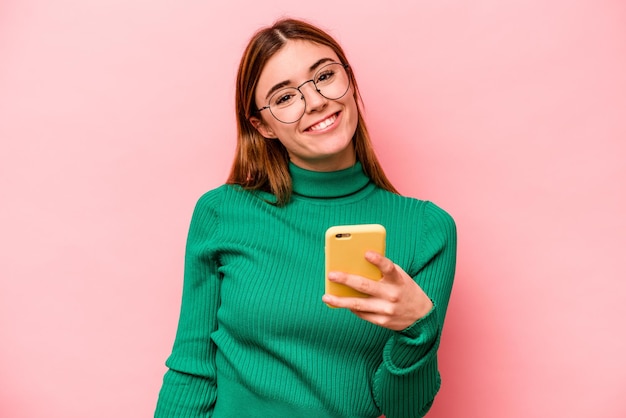 Jonge blanke vrouw met mobiele telefoon geïsoleerd op roze achtergrond gelukkig lachend en vrolijk