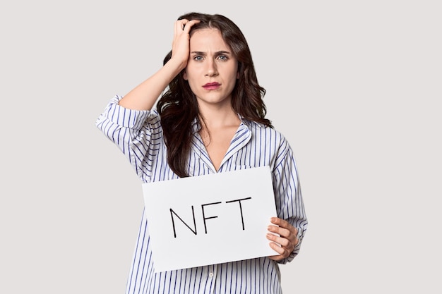 Jonge blanke vrouw met 'NFT' banner in de studio wordt geschokt ze heeft zich een belangrijke vergadering herinnerd