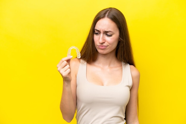 Jonge blanke vrouw met onzichtbare accolades geïsoleerd op gele achtergrond met droevige uitdrukking