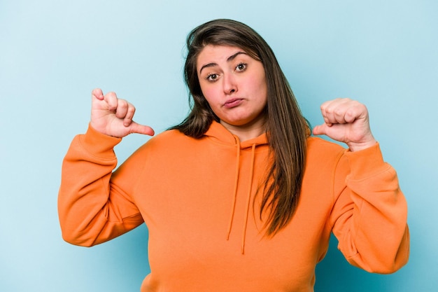 Jonge blanke vrouw met overgewicht geïsoleerd op blauwe achtergrond voelt zich trots en zelfverzekerd voorbeeld om te volgen