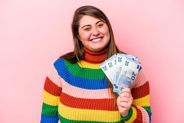 Jonge blanke vrouw met overgewicht met bankbiljetten geïsoleerd op roze achtergrond gelukkig, glimlachend en vrolijk.