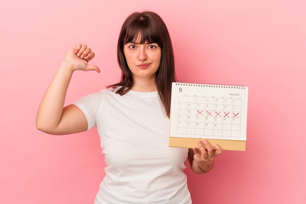 Jonge blanke vrouw met overgewicht met kalender geïsoleerd op roze achtergrond voelt zich trots en zelfverzekerd, voorbeeld om te volgen.