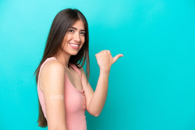 Jonge blanke vrouw met pleisters geïsoleerd op een blauwe achtergrond die naar de zijkant wijst om een product te presenteren