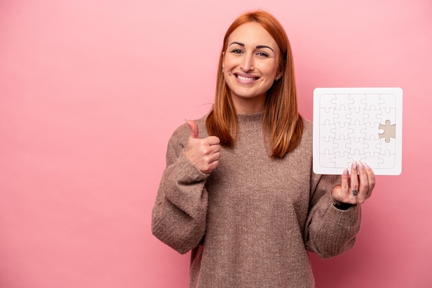 Jonge blanke vrouw met puzzel geïsoleerd op roze achtergrond glimlachend en duim omhoog