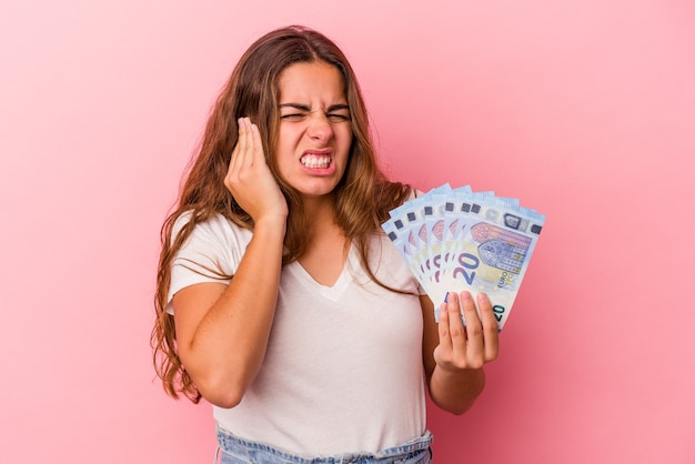 Jonge blanke vrouw met rekeningen geïsoleerd op een roze achtergrond die oren bedekt met handen.