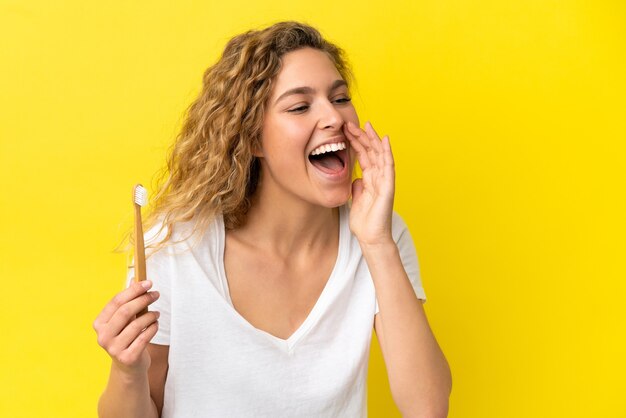 Jonge blanke vrouw met tandenpoetsen geïsoleerd op gele achtergrond schreeuwend met mond wijd open naar de zijkant open