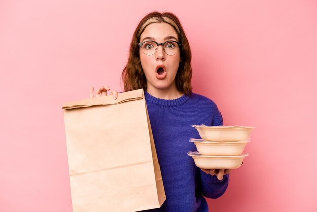 Jonge blanke vrouw met tupperware en afhaalmaaltijden tas geïsoleerd op roze achtergrond