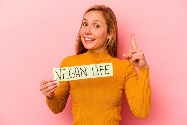 Jonge blanke vrouw met veganistisch leven plakkaat geïsoleerd op roze achtergrond