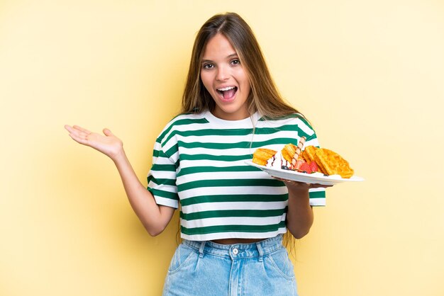 Jonge blanke vrouw met wafels geïsoleerd op gele achtergrond met geschokte gezichtsuitdrukking