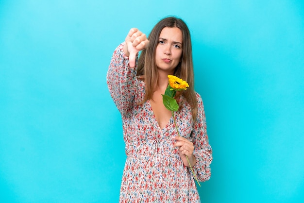 Jonge blanke vrouw met zonnebloem geïsoleerd op blauwe achtergrond met duim naar beneden met negatieve uitdrukking