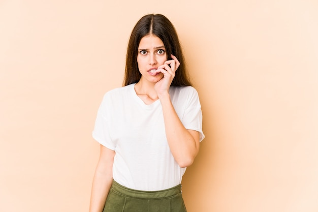 Jonge blanke vrouw op beige muur bijten nagels, nerveus en erg angstig.