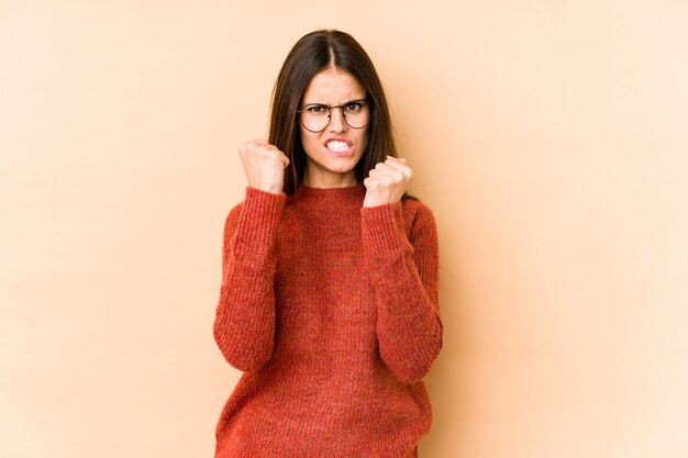 Jonge blanke vrouw op beige muur boos schreeuwen met gespannen handen.