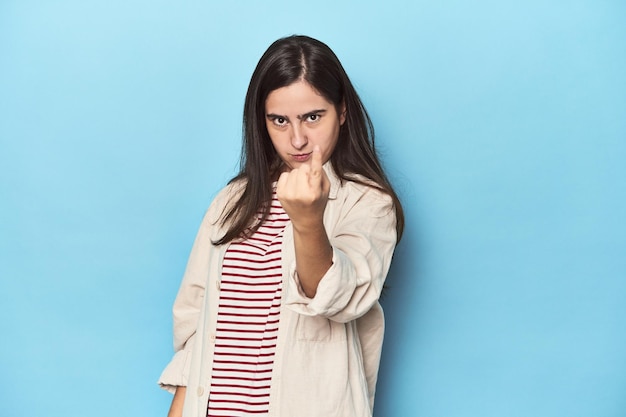 Jonge blanke vrouw op blauwe achtergrond wijst met de vinger naar je alsof je uitnodigt om dichterbij te komen