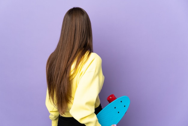 Jonge blanke vrouw op paarse muur met een skate in achterste positie