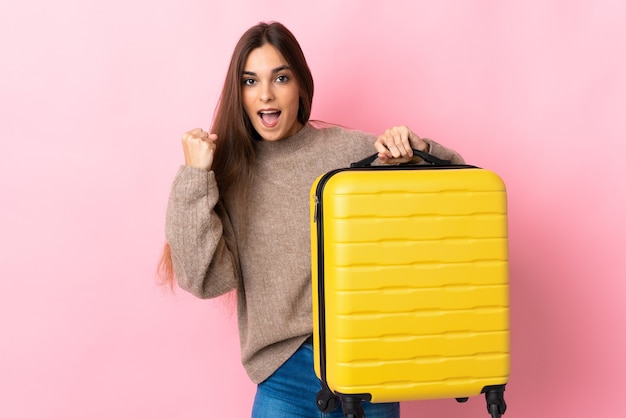 Jonge blanke vrouw op roze in vakantie met reiskoffer