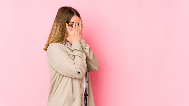 Jonge blanke vrouw op roze muur knipperen door angstige en nerveuze vingers.