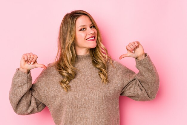 Jonge blanke vrouw op roze muur voelt zich trots en zelfverzekerd