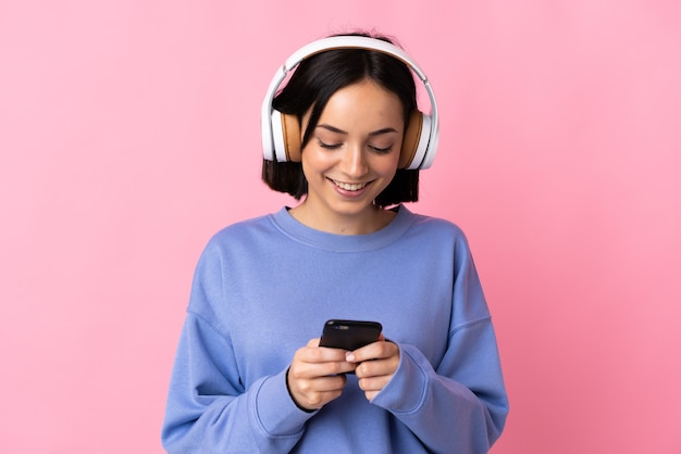 Jonge blanke vrouw op roze muziek luisteren en op zoek naar mobiel
