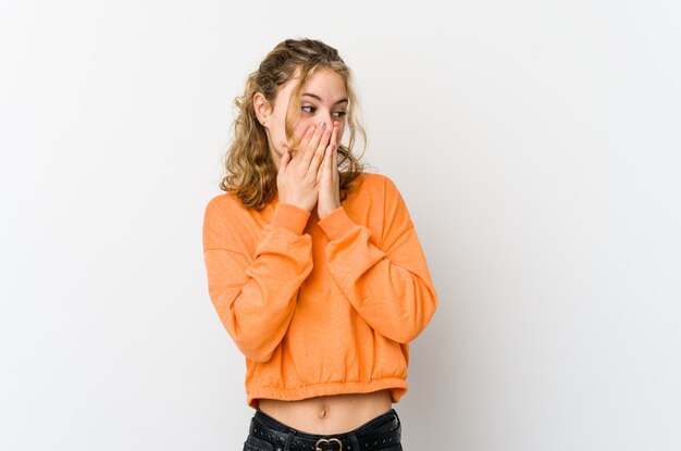 Jonge blanke vrouw op witte achtergrond lachen om iets, mond bedekken met handen.