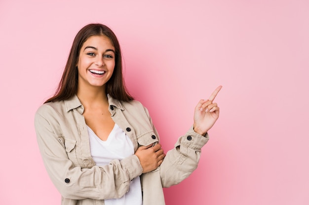 Jonge blanke vrouw poseren in een roze muur glimlachend vrolijk wijzend met wijsvinger weg.