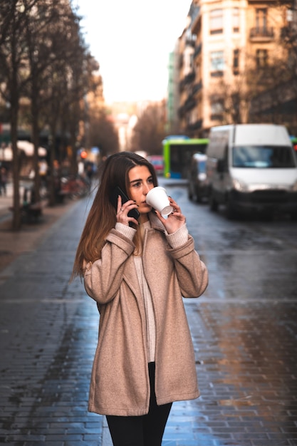 Jonge blanke vrouw praten via de telefoon terwijl het drinken van koffie