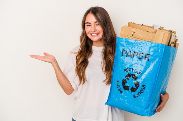 Jonge blanke vrouw recycling papier geïsoleerd op een witte achtergrond met een kopie ruimte op een palm en met een andere hand op de taille.