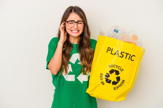 Jonge blanke vrouw recycling van een vol plastic geïsoleerd op een witte achtergrond die oren met handen bedekt.