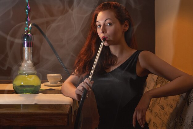 Jonge blanke vrouw rookt een waterpijp of shisha in de nachtclub of bar rook.