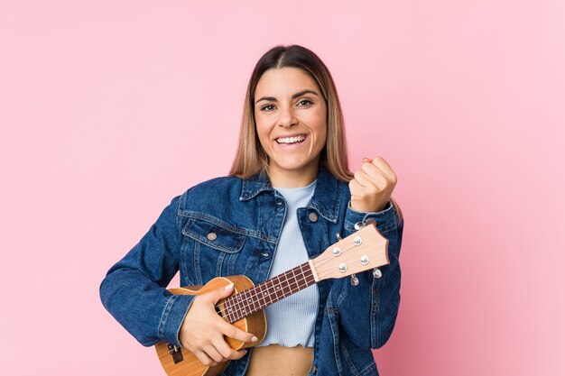 Jonge blanke vrouw spelen ukelele zorgeloos en opgewonden juichen.