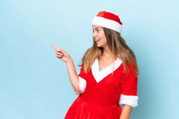 Jonge blanke vrouw verkleed als mama noel geïsoleerd op een blauwe achtergrond wijzende vinger naar de zijkant en presenteren van een product