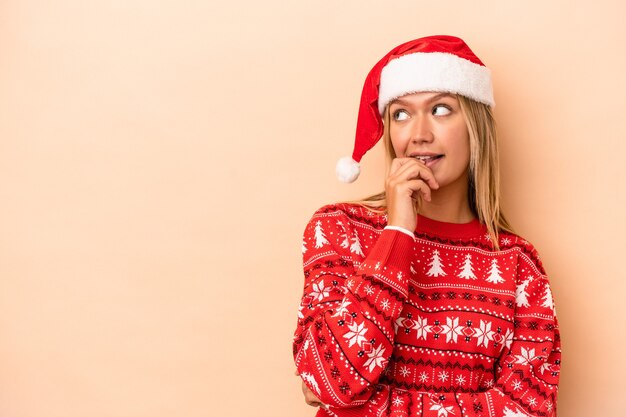 Jonge blanke vrouw viert Kerstmis geïsoleerd op beige achtergrond ontspannen denken over iets kijken naar een kopie ruimte.