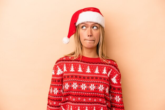 Jonge blanke vrouw viert kerstmis geïsoleerd op beige achtergrond verward, voelt zich twijfelachtig en onzeker.