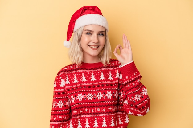 Jonge blanke vrouw viert Kerstmis geïsoleerd op gele achtergrond vrolijk en zelfverzekerd met ok gebaar.