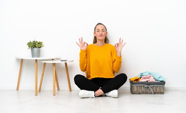 Jonge blanke vrouw vouwen kleding zittend op de vloer geïsoleerd op een witte achtergrond in zen pose