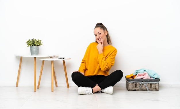 Jonge blanke vrouw vouwen kleding zittend op de vloer geïsoleerd op een witte achtergrond