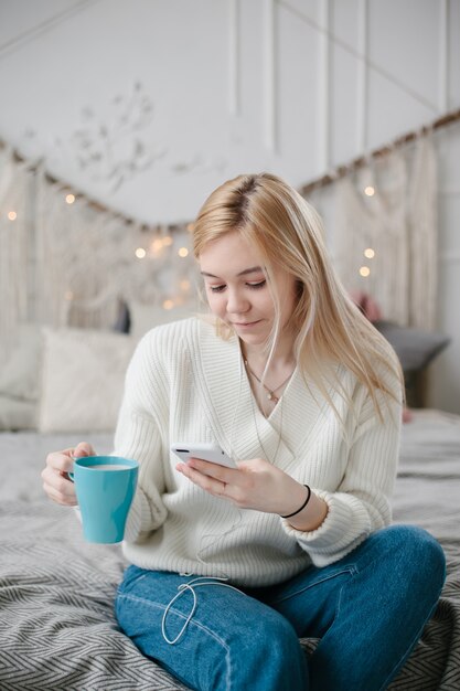 Jonge blanke vrouw zit op bed en gebruikt een smartphone