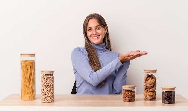 Jonge blanke vrouw zittend aan een tafel met voedselpot geïsoleerd op een witte achtergrond met een kopie ruimte op een palm.