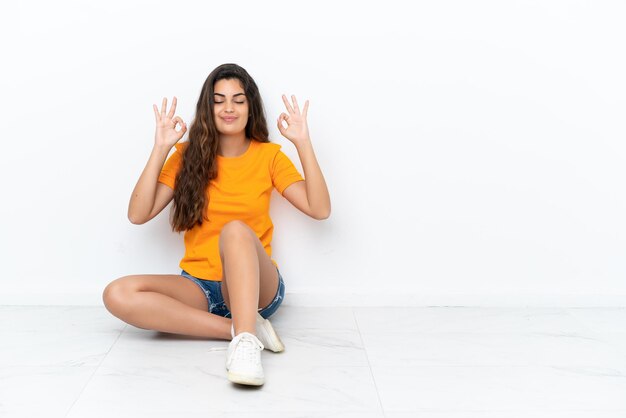 Jonge blanke vrouw zittend op de vloer geïsoleerd op een witte achtergrond in zen pose