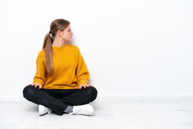 Jonge blanke vrouw zittend op de vloer geïsoleerd op een witte achtergrond in zijpositie