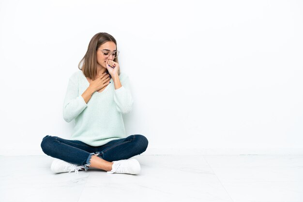 Jonge blanke vrouw zittend op de vloer geïsoleerd op een witte achtergrond lijdt aan hoest en voelt zich slecht