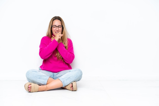 Jonge blanke vrouw zittend op de vloer geïsoleerd op een witte achtergrond lijdt aan hoest en voelt zich slecht