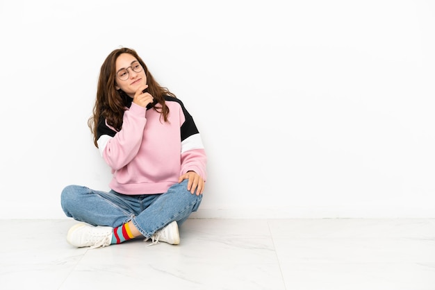 Jonge blanke vrouw zittend op de vloer geïsoleerd op een witte achtergrond op zoek naar de zijkant