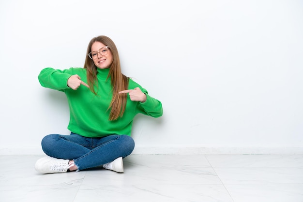 Jonge blanke vrouw zittend op de vloer geïsoleerd op een witte achtergrond trots en zelfvoldaan