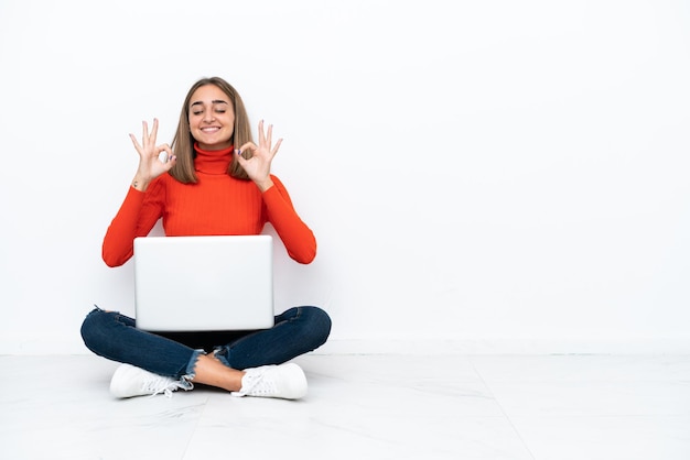 Jonge blanke vrouw zittend op de vloer met een laptop in zen pose