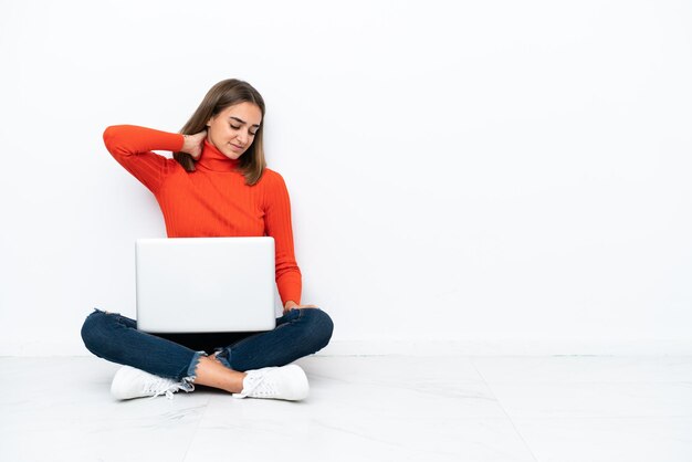 Jonge blanke vrouw zittend op de vloer met een laptop met nekpijn