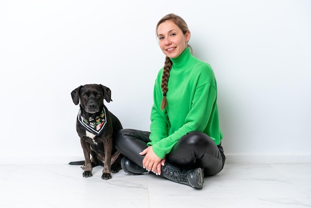 Jonge blanke vrouw zittend op de vloer met zijn puppy geïsoleerd op een witte achtergrond die veel lacht