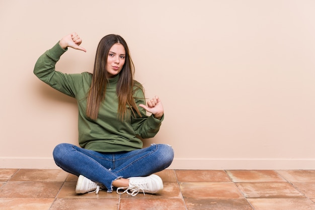 Jonge blanke vrouw zittend op de vloer voelt zich trots en zelfverzekerd, voorbeeld te volgen.